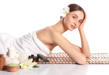 Beyaz arka planda bambu hasırında poz veren güzel bir kadın. Ayna yüzeyinde kaplıca ürünleri ve çiçekler