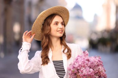 Gülümseyen kadın, bulanık arka planda bir demet leylak çiçeğiyle.