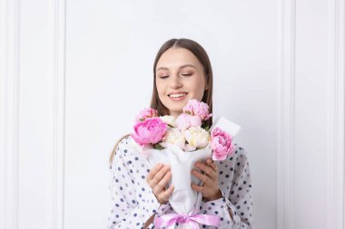 Beyaz duvarın yanında şakayık demeti olan güzel bir kadın.