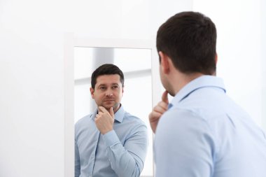 Yakışıklı adam aynada kendine bakıyor.