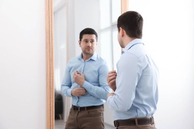 Yakışıklı adam aynada kendine bakıyor.