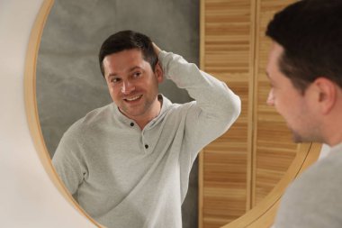 Yakışıklı adam aynada kendine bakıyor.