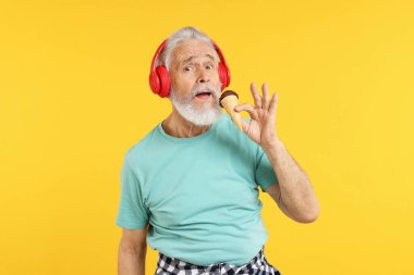 Kulaklıklı, turuncu arka planda dondurmalı yaşlı bir adam.