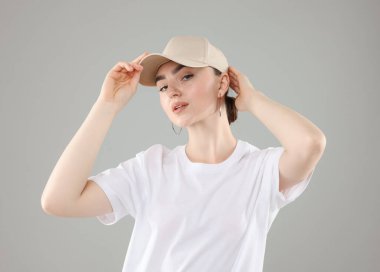 Gri arka planda şık beyzbol şapkalı güzel bir kadın.