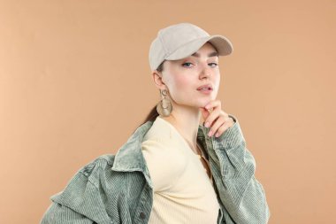 Bej arka planda şık bir beyzbol şapkası takmış güzel bir kadının portresi.