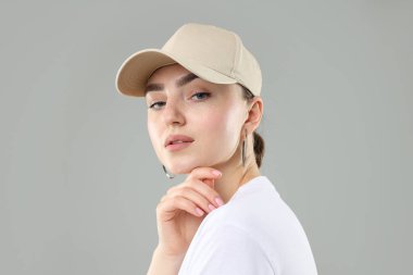 Gri arka planda şık beyzbol şapkalı güzel kadın, yakın plan.