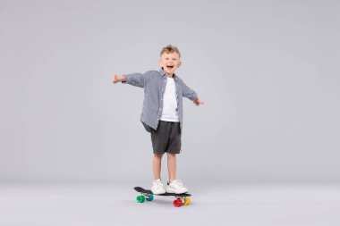 Neşeli küçük çocuk para tahtasının üzerinde duruyor ve gri arka planda baş parmak gösteriyor.