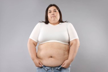 Gri arka planda aşırı göbek yağlı bir kadın. Aşırı kilolu