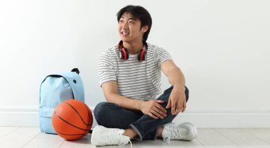 Kapalı alanda basketbol topu ve sırt çantası olan mutlu bir öğrenci.