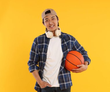 Kulaklıklı ve turuncu arka planda basketbol topu olan bir öğrenci.