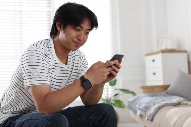 Evde akıllı telefonu olan yakışıklı Asyalı adam.