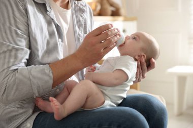 Babası evdeki kanepede bebeğini biberonla besliyor.
