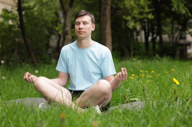 Genç adam parkta yoga yapıyor.