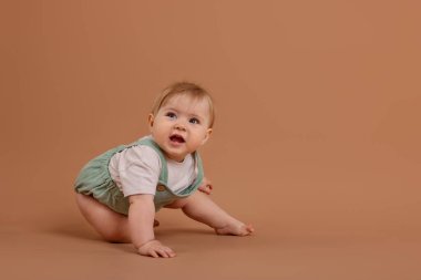 Soluk kahverengi arka planda emekleyen şirin küçük bebek, mesaj için yer var.