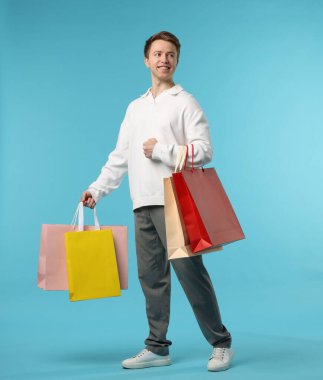 Açık mavi arka planda alışveriş torbaları olan neşeli bir adam.