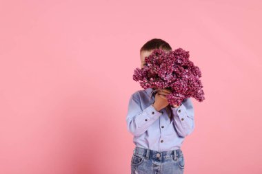 Pembe arka planda bir buket leylak çiçekli küçük çocuk, mesaj için yer var.