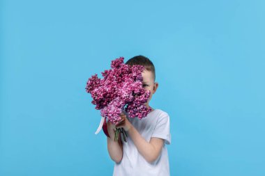 Açık mavi arka planda bir buket leylak çiçekli küçük çocuk.