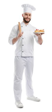 Üniformalı mutlu pastacı elinde çilekli lezzetli profiteroller ve beyaz arka planda merdane tutuyor.