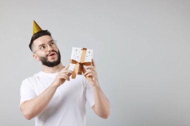 Doğum günün kutlu olsun. Gri arka planda parti şapkası ve hediye kutusu olan yakışıklı bir adam.