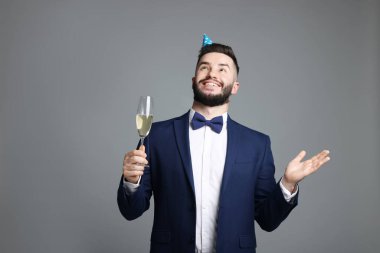 Doğum günün kutlu olsun. Gri arka planda parti şapkası ve şampanya kadehi olan yakışıklı bir adam.