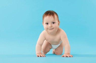 Açık mavi arka planda emekleyen şirin bir bebek.