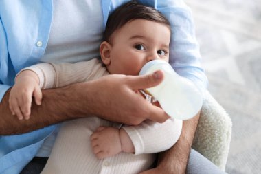 Babası küçük bebeğini evdeki koltukta biberonla besliyor.