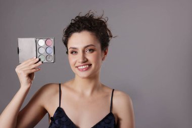 Gri arka planda göz farı paleti olan gülümseyen bir kadın. Metin için boşluk