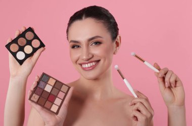 Göz farı paletleri, fırçalar ve pembe arka planda gülümseyen bir kadın olan makyaj sanatçısı.