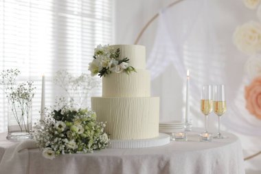 Çiçek desenli nefis düğün pastası, çiçek buketi ve kapalı bir masada bir bardak şampanya.