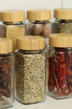 Beyaz masadaki kavanozlardaki farklı aromatik baharatlar, yakın plan.