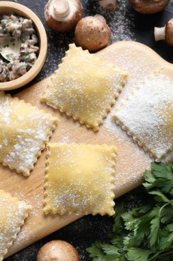 Pişmemiş ravioli ve mantarlar siyah masada, yakın plan.