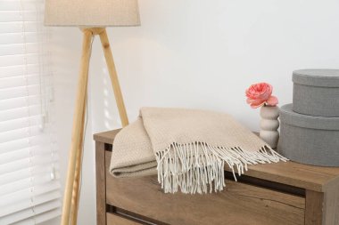 Bej renkli yün battaniye, kutular, vazodaki güzel çiçek çekmecelerden yapılmış tahta sandık ve beyaz duvarın yanındaki lamba, yakın plan.