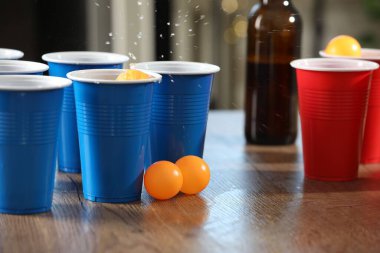 Bira pong oyunu. İçkili plastik bardaklar ve toplar ahşap masada, yakın plan.