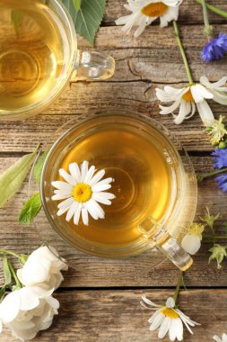 Cam fincanlarda aromatik bitki çayı ve tahta masada çiçekler.