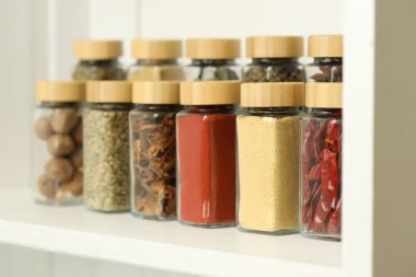 Kapalı alandaki beyaz raflardaki kavanozlardaki farklı aromatik baharatlar.