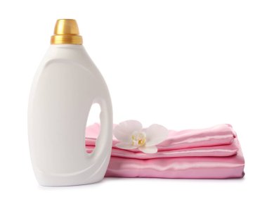 Bir şişe yumuşatıcı, üst üste yığılmış giysiler ve beyaz bir çiçek.