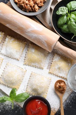 Pişmemiş ravioli, merdane, bolonez, sos ve fesleğen siyah masada, düz yatıyordu.