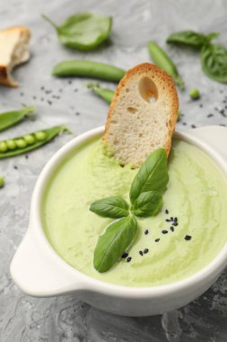 Lezzetli bezelye kremalı çorba fesleğen ve kızarmış ekmek, yakın plan, gri masada servis edilir.