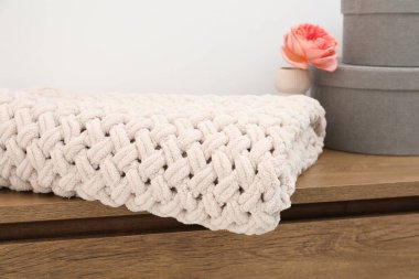 Yünlü battaniye, kutular ve vazodaki güzel çiçek beyaz duvarın yanındaki ahşap sandıkta, yakın plan.