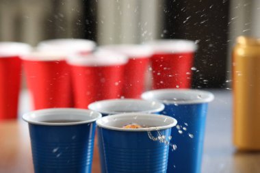 Bira pong oyunu. İçkili plastik bardaklar ve masada top, yakın plan.