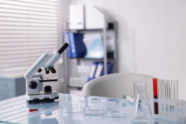Laboratuvardaki beyaz masada, petri kabı, mikroskop ve test tüpleri.