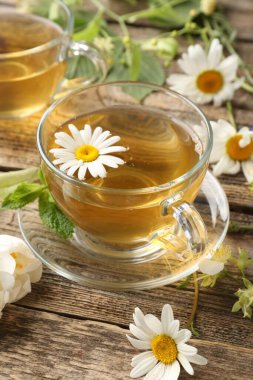 Cam bardaklarda aromatik bitki çayı, ahşap masada nane ve çiçekler, yakın plan.