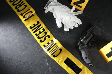 Adli tıp uzmanı. Sarı olay yeri bandı, işaretler, eldivenler ve silah siyah masanın üstünde, görüş alanının üstünde. Metin için boşluk