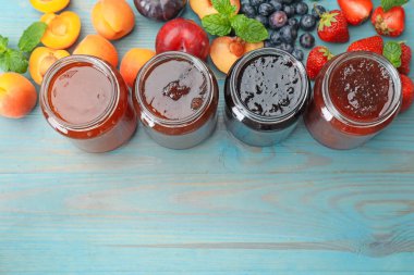 Kavanozlardaki farklı reçeller ve mavi ahşap masa üzerindeki malzemeler düz. Metin için boşluk