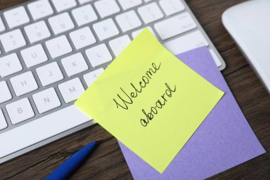 Kağıt not cümlesiyle Gemiye hoş geldiniz, kalem ve klavye ahşap masa, yakın plan