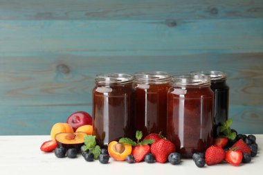 Kavanozlardaki farklı reçeller ve beyaz masadaki malzemeler. Metin için boşluk