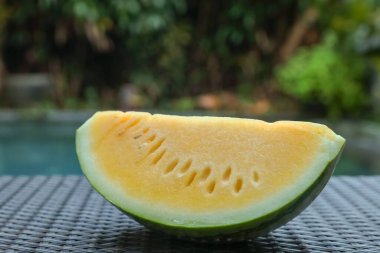 Açık havuz kenarında hasır masada lezzetli bir karpuz dilimi, yakın plan.