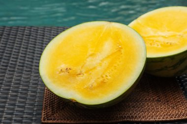 Yüzme havuzunun yakınındaki hasır masada olgun sarı karpuz parçaları.