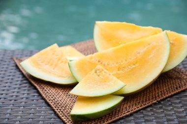 Olgun sarı karpuz parçaları hasır masada, yüzme havuzunun yanında, yakın plan.