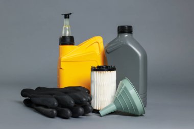 Plastik kaplarda motor yağı, filtre, eldivenler ve gri arka planda huni